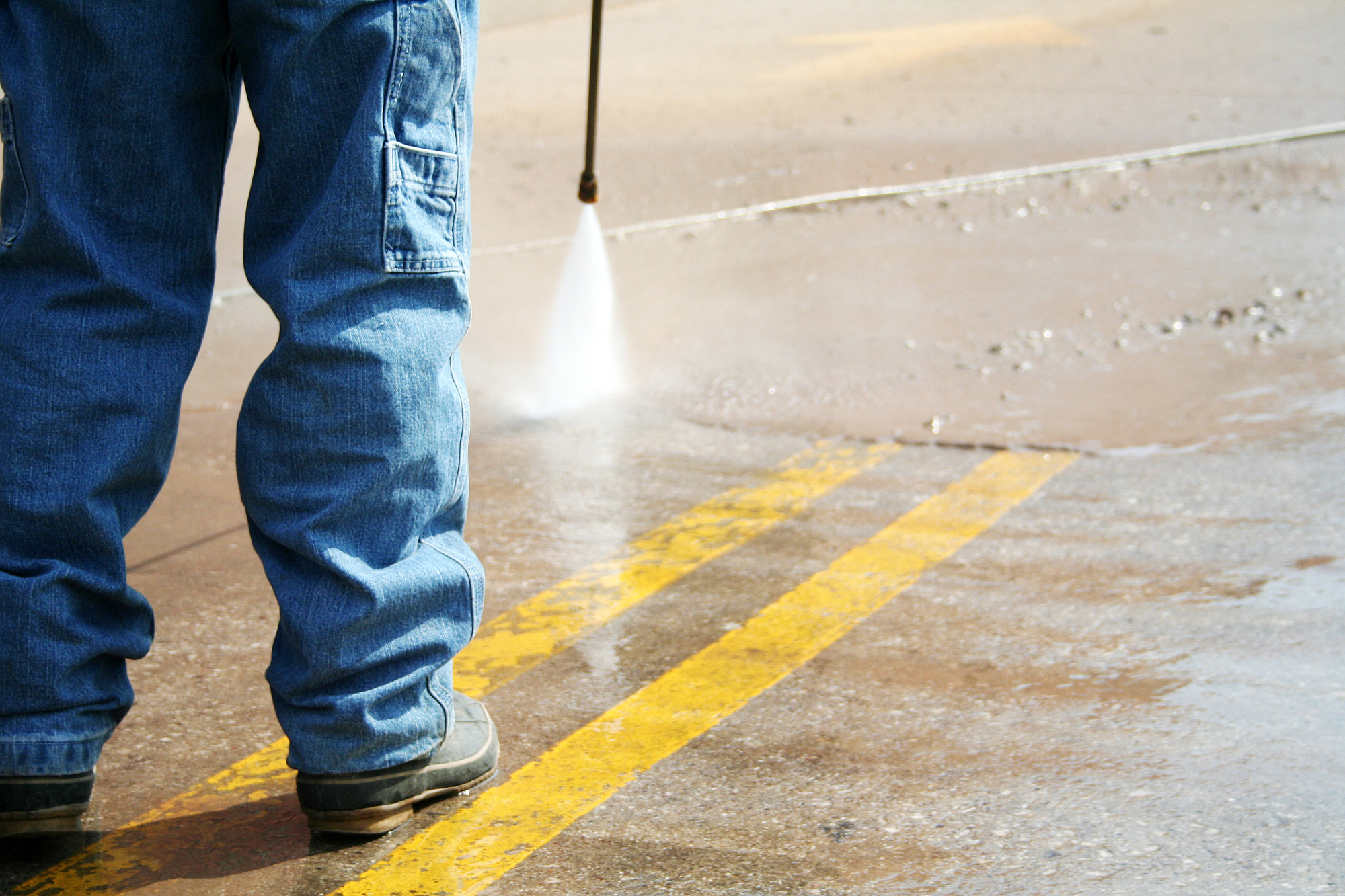 A Person Cleaning a Road With a Pressure Washer